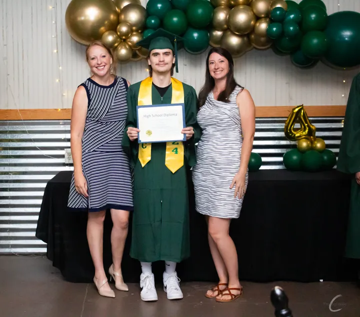 A Northshore HTC graduate in cap and gown holding their high school diploma, celebrating with family