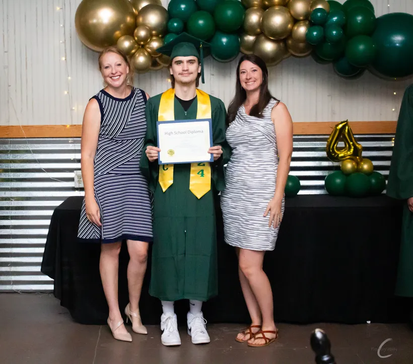 A Northshore HTC graduate in cap and gown holding their high school diploma, celebrating with family