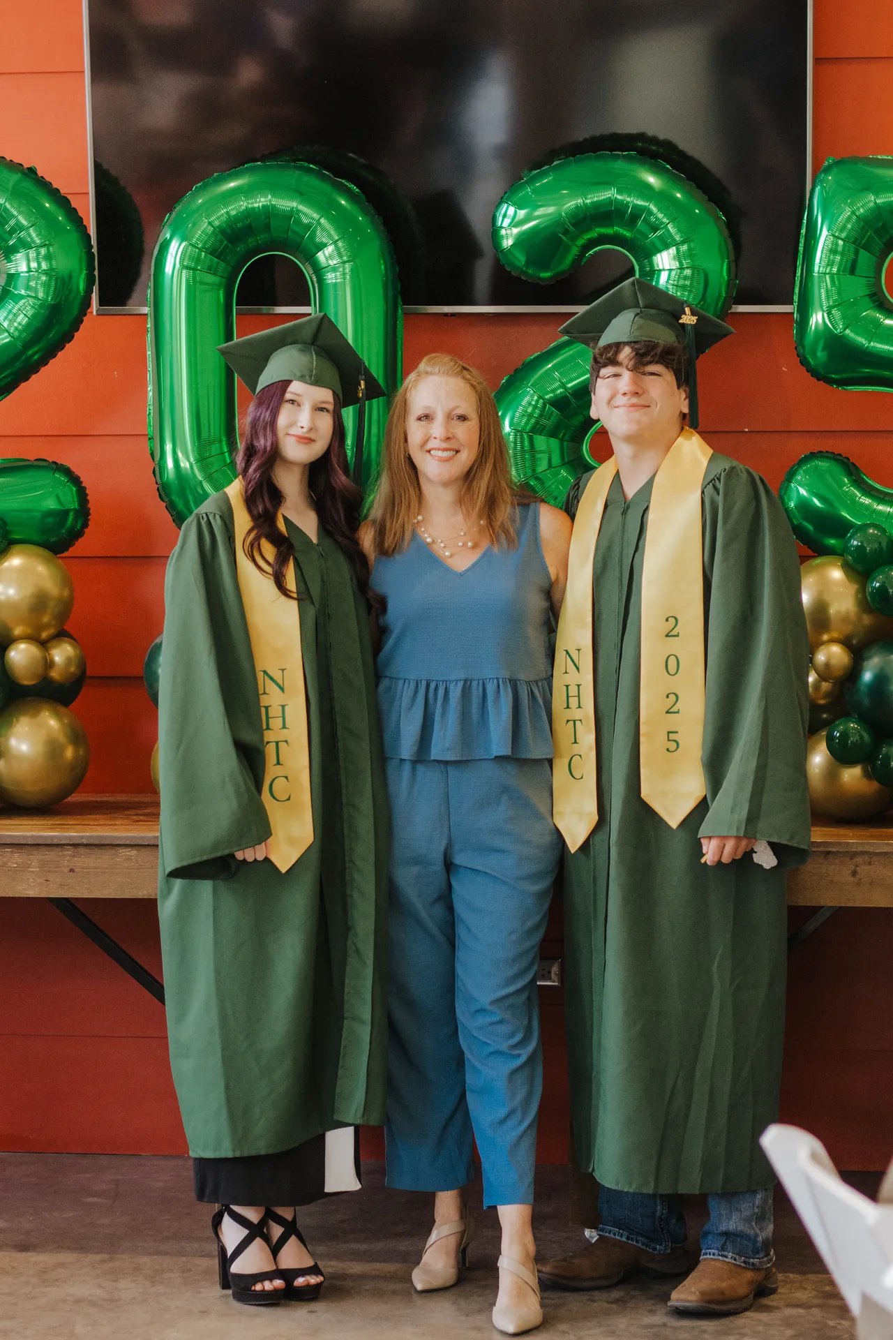 Two graduates in gold NHTC stoles celebrating with their teacher