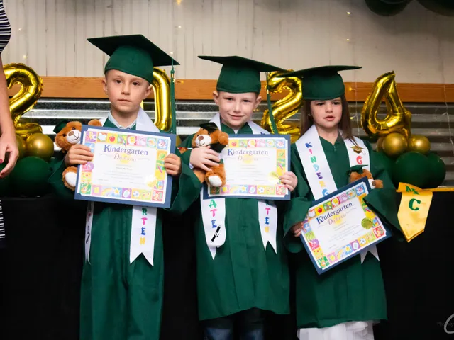 Three kindergarten graduates in tiny caps and gowns holding certificates