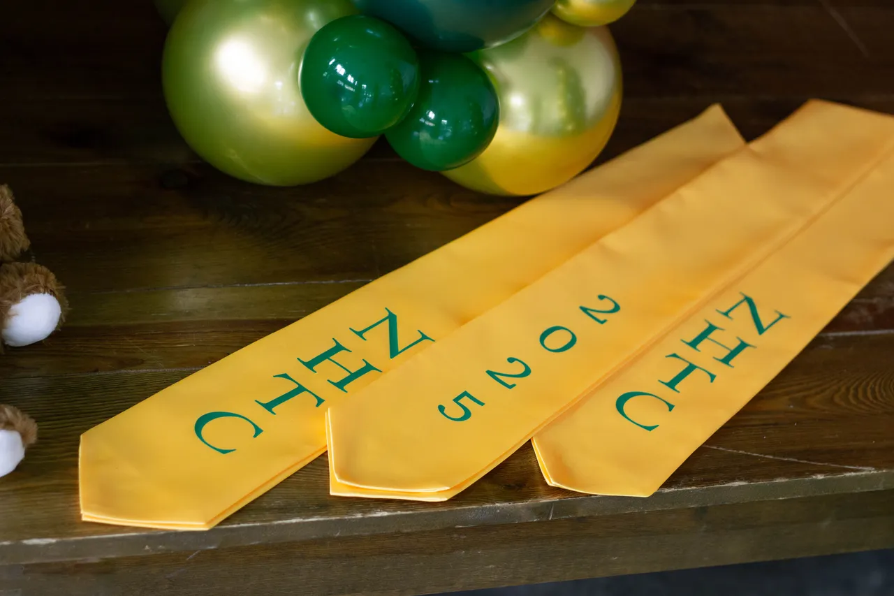 Gold NHTC graduation stoles laid out beside green and gold balloons