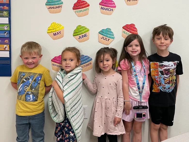 Smiling Pre-K students lined up in their classroom beneath a colorful months-of-the-year wall display