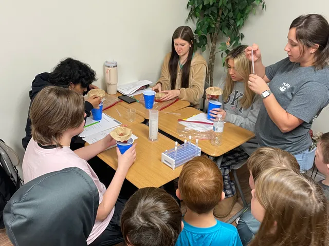 A mixed-age science class gathered around a table for an experiment